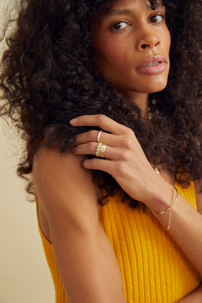 woman wearing moderately textured gold band with straight sides alongside other gold jewelry