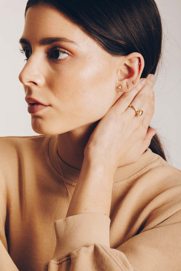 woman wearing gold square with round white diamond stud earring alongside other gold jewelry