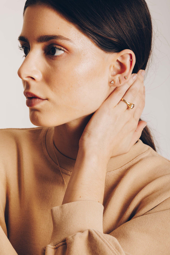 woman wearing gold square with round white diamond stud earring alongside other gold jewelry